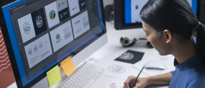 A graphic designer uses a computer, pen and paper to create a design